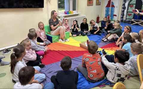 Dzieci siedzą z bibliotekarką na chuście animacyjnej, bibliotekarka pokazuje ksiązkę