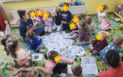 Bibliotekarka wspólnie z dziećmi siedzi na dywanie