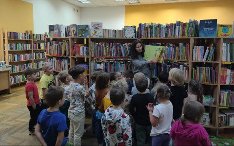 Dziewczynka wraz z bibliotekarkami pokazuje książkę i zakładkę