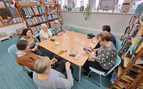 Seniorki siedzą przy stole i chwalą się technikami rękodzielniczymi