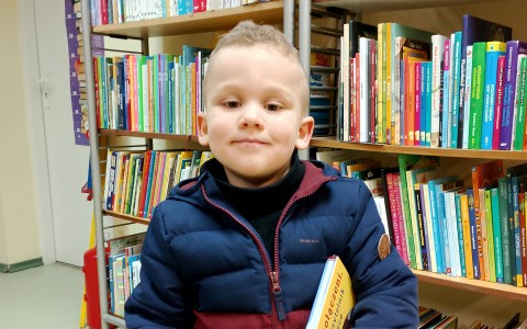 Zdjęcie przedstawia chłopca trzymającego wyprawkę czytelnika: książkę, kartę czytelnika i zakładkę