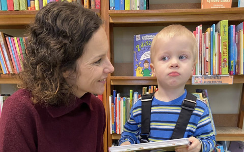 Bibliotekarka patrzy na chłopca. Chłopiec trzyma ksiązkę. W tle widać regał z książkami