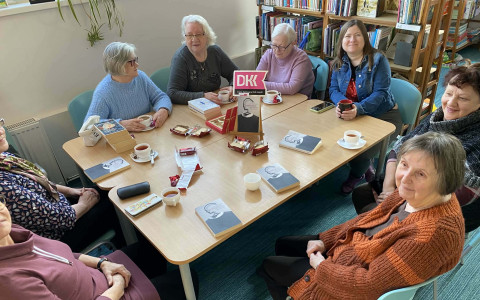 seniorki siedzą przy stole i dyskutują z bibliotekarka o przeczytanej książki