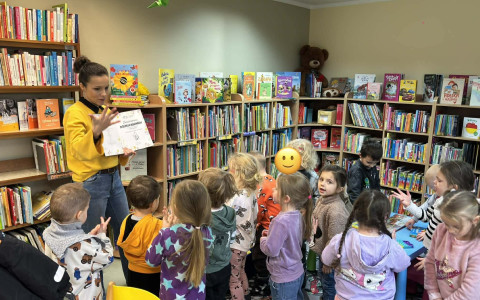 Bibliotekarka trzyma książkę a dzieci stoją wokół niej.