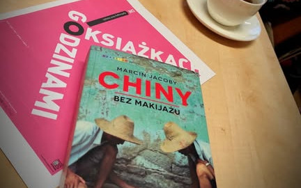 Na kartce z logo DKK połozona książka Marcina Jacoby pt. " Chiny bez makijażu", w tle filiżanka z kawą.