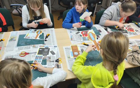 Pięć dziewczynek siedzi przy stole i wycina modele z papieru