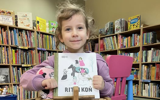 Dziewczynka trzyma książkę i uśmiecha się do zdjęcia