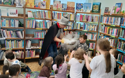Pan z Pomysłowej Fabryki wykonuje eksperymenty podczas zajęć z dziećmi w bibliotece