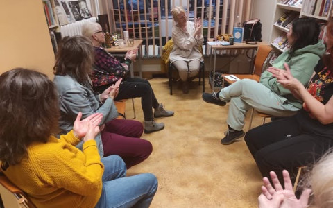 Prowadząca  pokazuje uczestniczkom warsztatów jak masować dłoń, Panie również masują swoje dłonie.