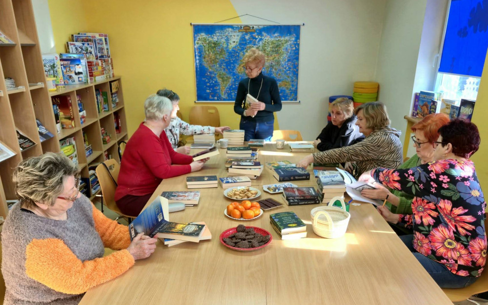 Na zdjęciu uczestniczki spotkania siedzą przy stołach i przeglądają przygotowane dla nich nowości książkowe.