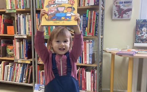 Dziewczynka prezentuje książkę, którą wybrała. Trzyma ją w górze.