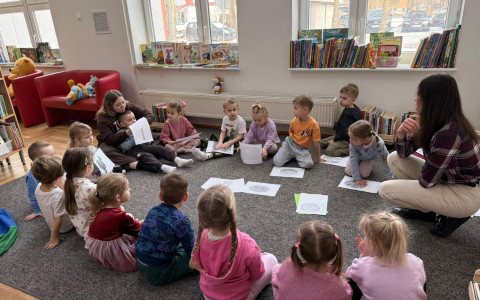 Bibliotekarka pokazuje dzieciom obrazki, a dzieci siedzą w kole na dywanie