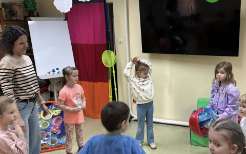 Dzieci w trakcie zabawy z panią bibliotekarką. Dzieci stoją w kółku i podają sobie piłkę