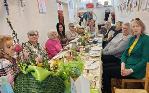 Panie z klubu gier planszowych siedzą przy zastawionym świątecznymi potrawami i stroikami stole.