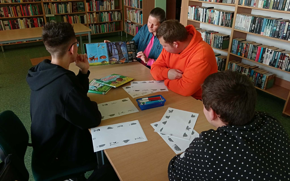 Bibliotekarka pokazuje uczestnikom zajęć książkę o lesie.