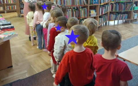 Dzieci stoją jeden za drugim, w tle książki