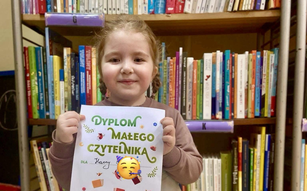 Dziewczynka trzyma dyplom i uśmiecha się do zdjęcia