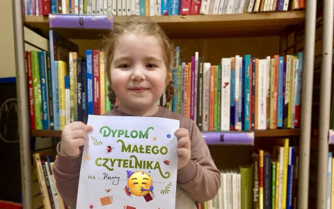 Dziewczynka trzyma dyplom i uśmiecha się do zdjęcia