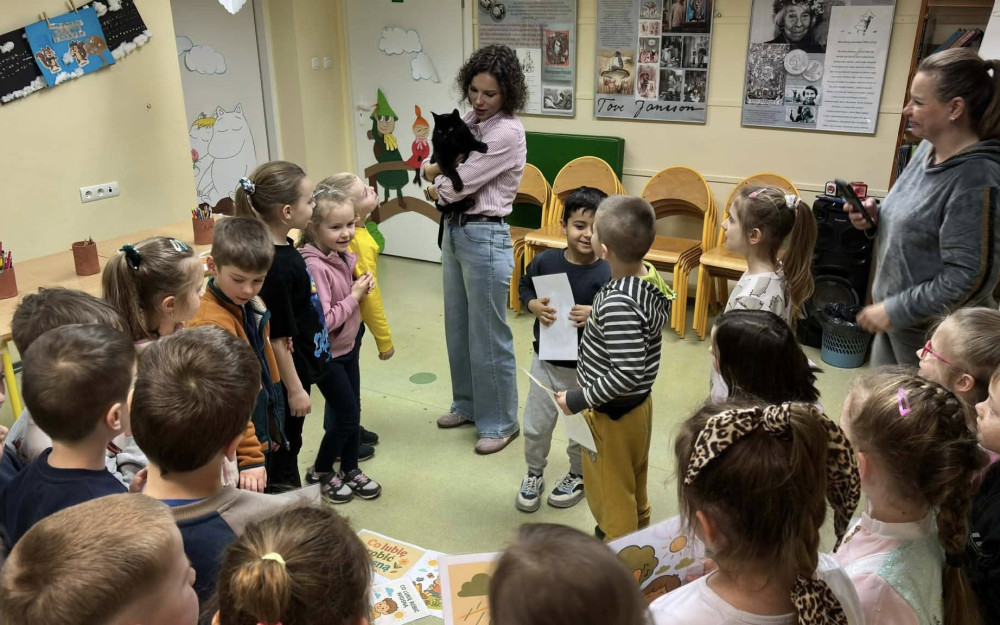 Bibliotekarka trzyma na rękach czarnego kota. dzieci stoją w kółku i cieszą sie do kota.