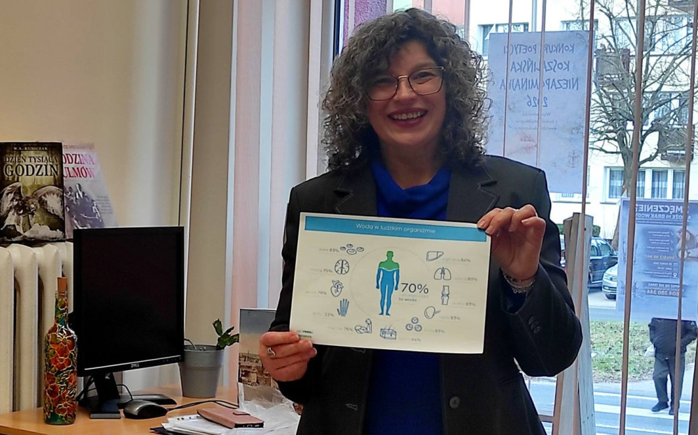 Wiesława Rudnik prezentująca  grafiką przedstawiającą poziom nawodnienia organizmu. Obok niej siedzi uczestniczka spotkania.