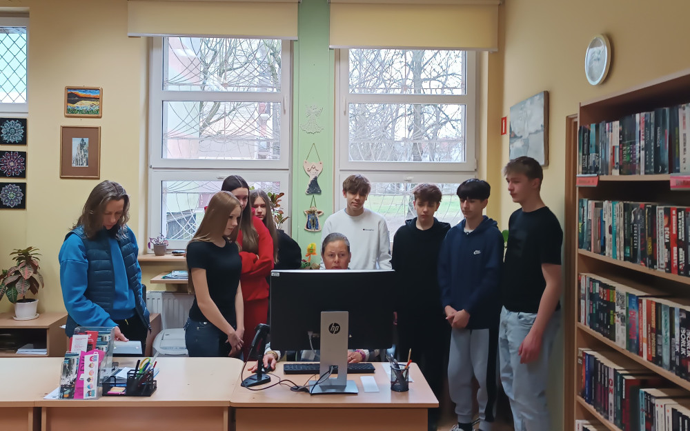 Bibliotekarka omawia uczniom proces wypożyczania książek w bibliotece.