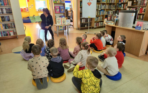 Na zdjęciu Wiola czyta siedzącym na podłodze przedszkolakom książkę o superbohaterach