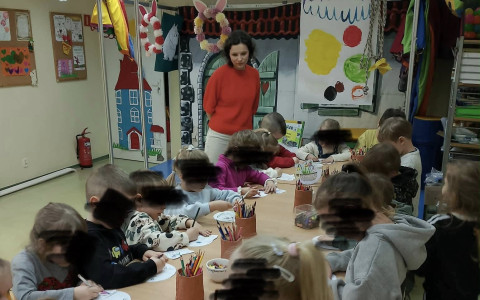 Dzieci stoją przy stolikach i wykonująprace plastyczne