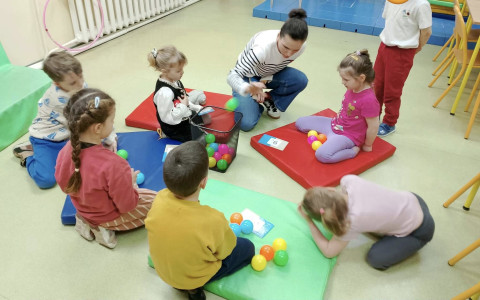 Dzieci siedzą na kolorowych materacykach i wraz z bibliotekarką przeliczają plastikowe piłeczki.