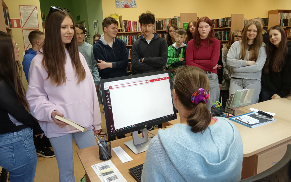 Bibliotekarka omawia uczniom proces wypożyczania książek w bibliotece.