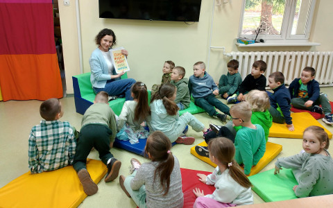 Bibliotekarka prezentuje wiosenne plansze. Dzieci siedzą na kolorowych materacykach