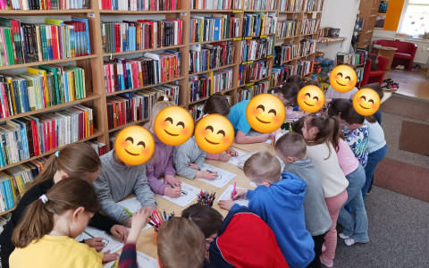 Dziecin stoją przy stolikach i wykonują pracę plastyczną
