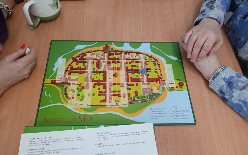 Na zdjęciu plansza do gry Koszalin MD i dwie pary dłoni