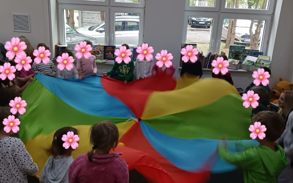 Dzieci stoją w kole i trzymają kolorową chustę animacyjną, podczas zabawy integracyjnej