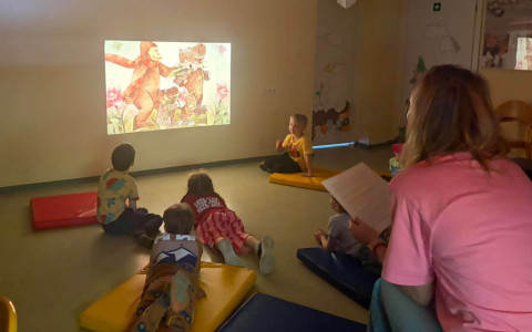 Bibliotekarka wyświetla dzieciom ilustrację na ścianie za pomocą projektorA i czyta baśń
