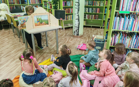 Przedszkolaki słuchają czytającej im bibliotekarki