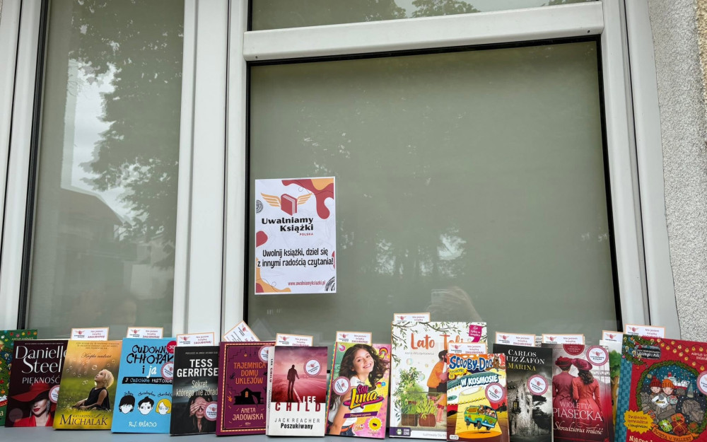 Książki stoją na parapecie, na szybie jest przyklejony plakat promujący akcje