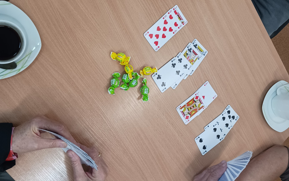 Na zdjeciu widoczne dwie pary dłoni, karty oraz dwie filiżanki z kawą