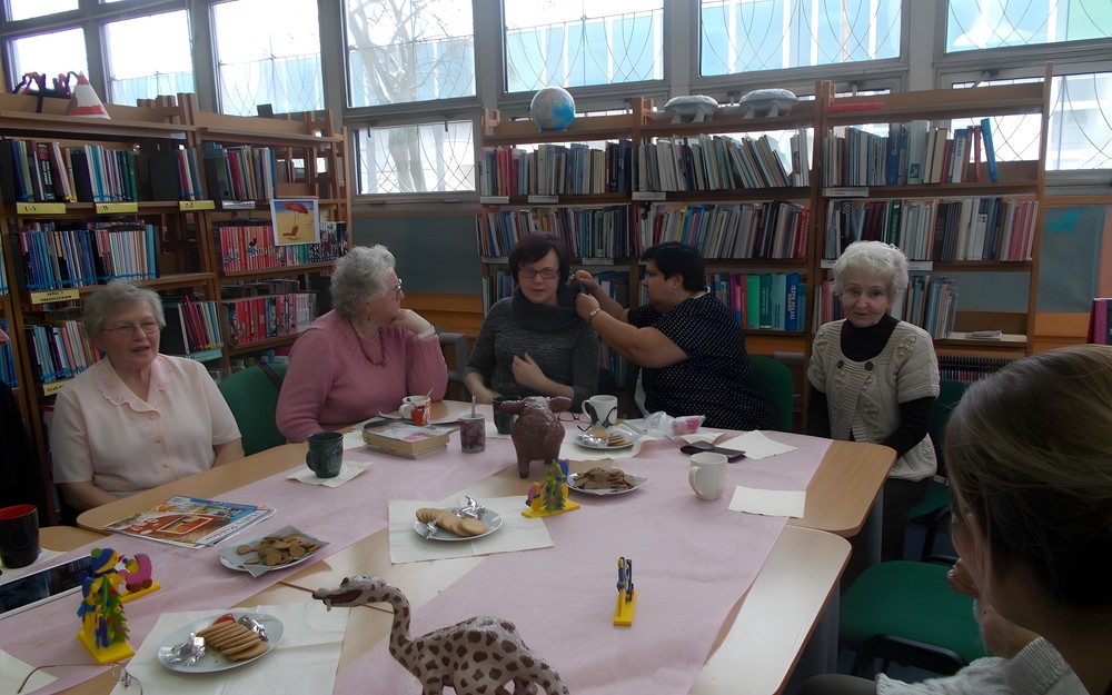 Panie siedzą przy stole i oglądają ręcznie robiony szal