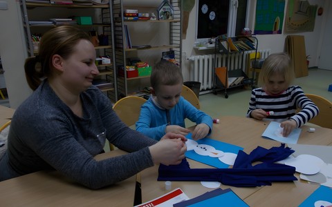 Zdjęcie przedstawia zajęcia dla młodszych czytelników. Do zajęć z dwojgiem tym razem dzieci, dołączyła jedna z mam. Na stole są kolorowe kartki, bibuła, klej nożyczki.