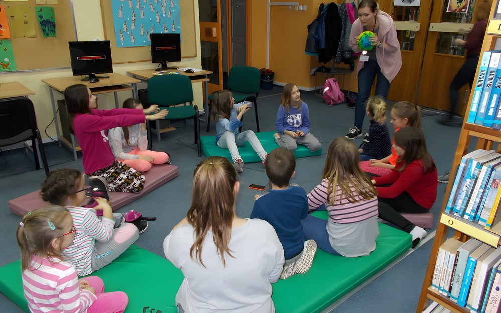 Bibliotekarka stoi przed dziećmi z piłką w ręku