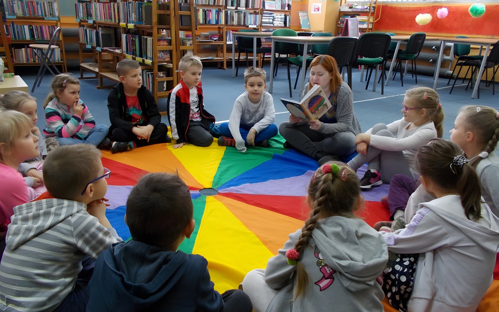 Bibliotekarka czyta książkę dzieciom siedzącym na chuście