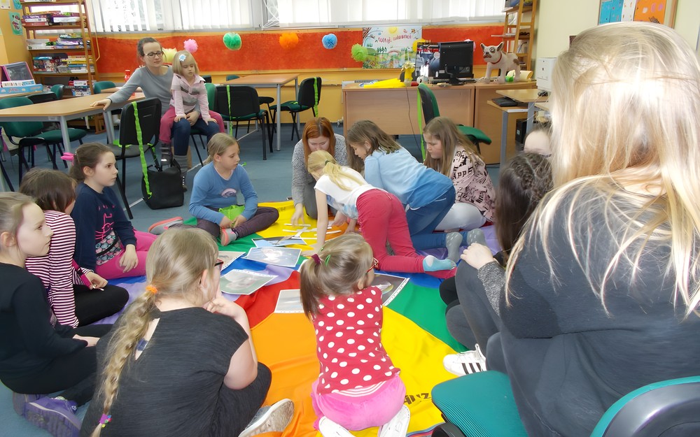 Dzieci wraz z bibliotekarką siedzą na chuście i dopasowują gotowe elementy