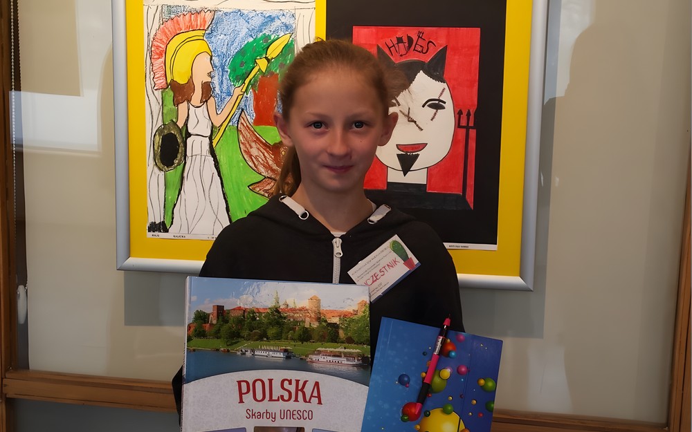 Dziewczynka stoi na tle prac plastycznych z nagrodą w ręku