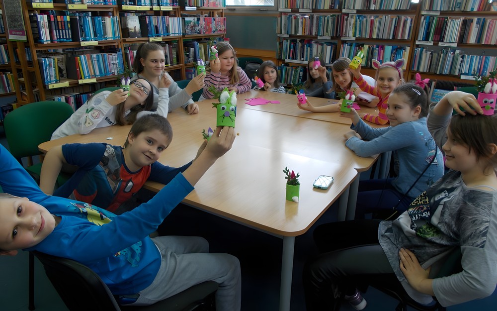 Dzieci siedzą przy stole pozując do zdjęcia z wykonanymi pracami plastycznymi