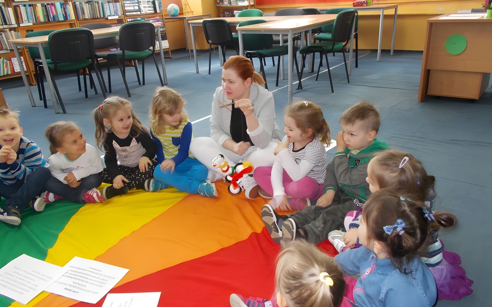Bibliotekarka pokazuje pacynkę dzieciom siedzącym na chuście
