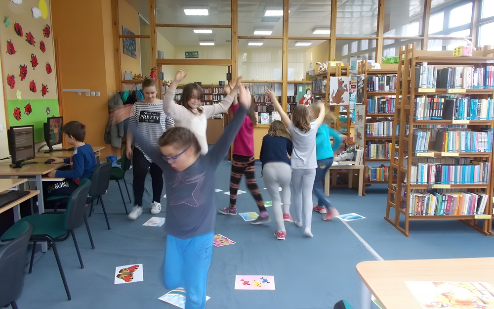 Dzieci tańczą wokół rozłożonych na ziemi ilustracji