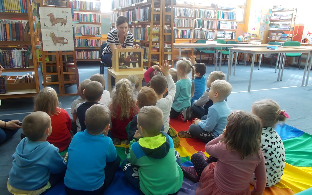Dzieci siedzą przed bibliotekarką, która czyta opowieść z kamishibai