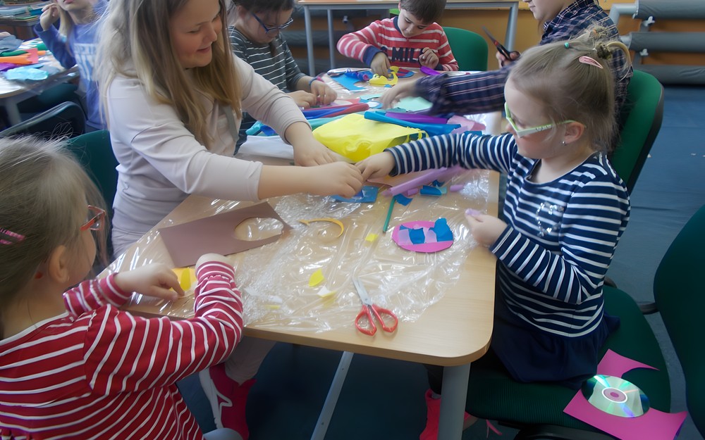 Dzieci siedzą przy stole i wycinają ryby z papieru