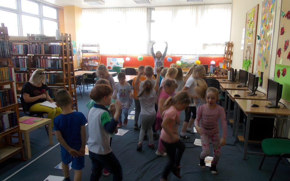 Dzieci tańczą zwrócone w stronę bibliotekarki pokazującej ruchy