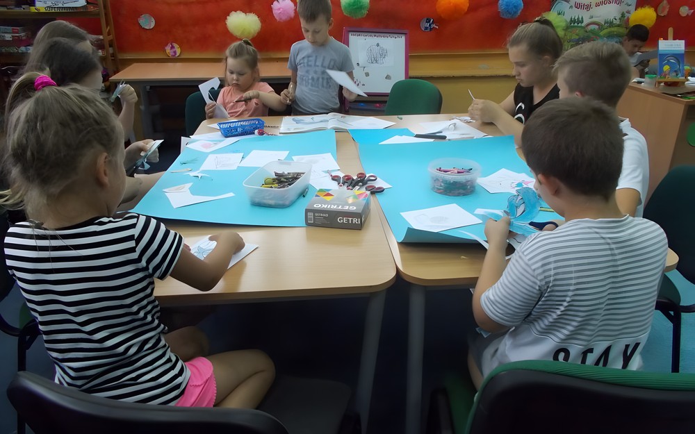 Dzieci siedzą przy stole i tworzą wspólny plakat